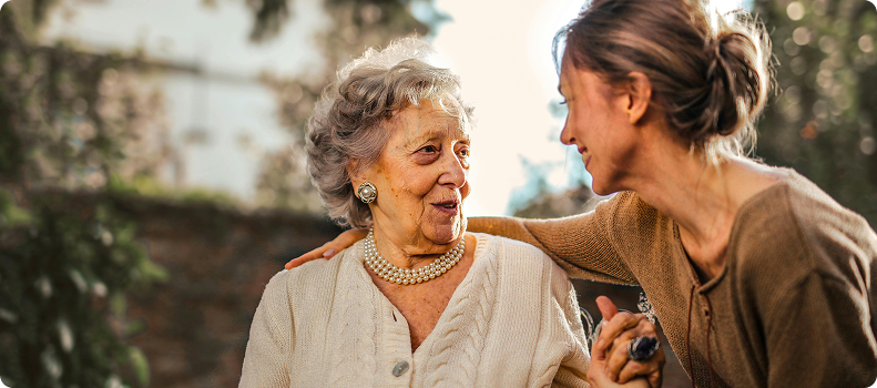 Mujer joven abrazando y sonriendo a una anciana en un ambiente al aire libre, ambas en una conversación afectuosa. Mujer joven abrazando y sonriendo a una anciana en un ambiente al aire libre, ambas en una conversación afectuosa.